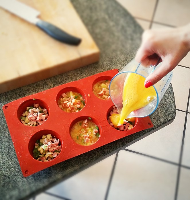 Riempimento degli stampi in silicone con i vari ingredienti: cacio, prosciutto cotto, asparagi, erba cipollina e uova sbattute.